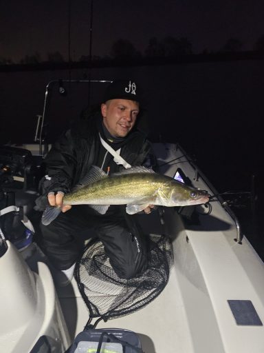 Mann hält einen großen Fisch auf einem Boot bei Nacht.